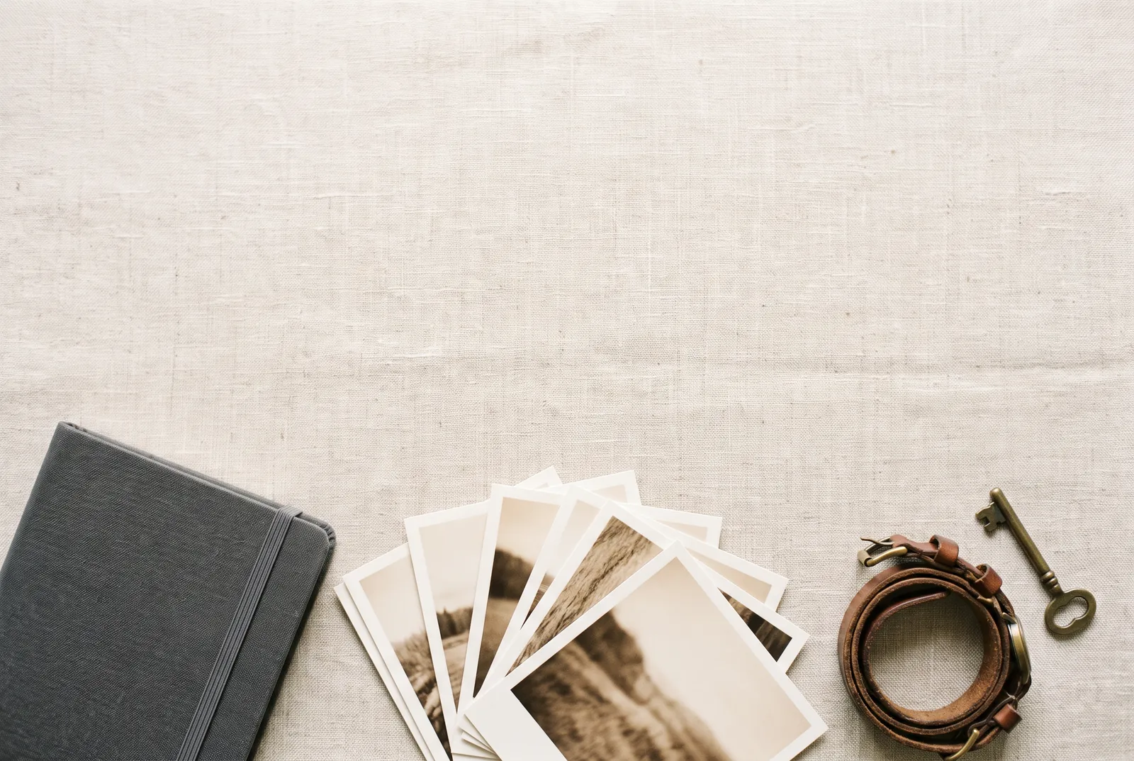 Photographs, a closed notebook, a watch strap and a small brass key laid on linen